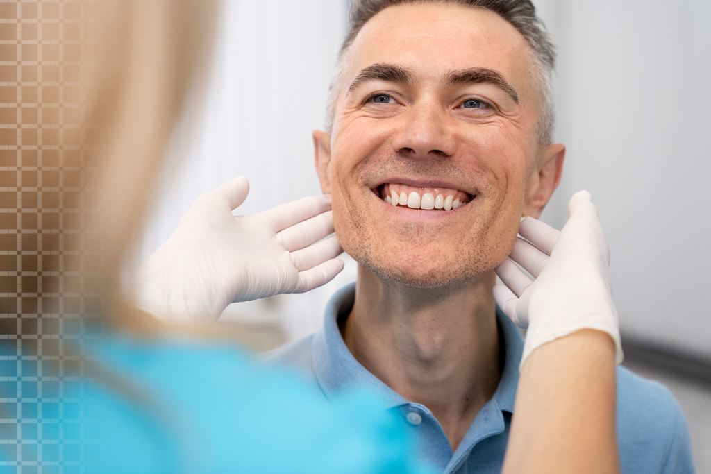 A happy male patient smiling confidently while a dentist, wearing gloves, examines his jaw after a successful dental implant procedure.